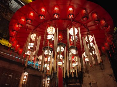 Bir Çin şehrinin sokaklarındaki eski bir binanın ortasında, parlak ışıklarla aydınlatılmış, sayısız beyaz ve açık sarı fenerle süslenmiş kırmızı dairesel bir tavan.