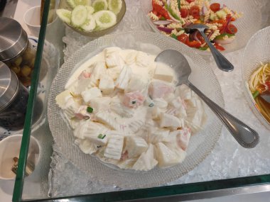 Bir havaalanı restoranındaki cam tezgahta salata ve makarnanın yanında kremalı soslu balık şeklinde bir şeker tabağı görülüyor. Ayrıca kasenin bir tarafında salatalık dilimleri var.