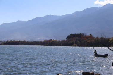 Dali 'nin güzel manzarası, sahildeki yunnan kışın göl suyu ve dağların sonsuz genişliğidir. Teknede balık tutan yalnız bir balıkçı var. Yanında da renkli ağaçlar var.