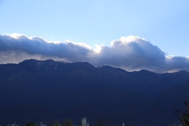 Sabahleyin, uzak dağların ardında sadece bir bulut var. Gökyüzünün mavi renginin üstünde ve altında birkaç bulut var.