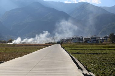 Asfalt yol çay tarlaları boyunca uzanıyor. Önünde ve arkasında sıcak buhar borularından yükselen beyaz dumanla Çin 'in yunnan eyaletindeki dağlarla çevrili antik bir kasaba var.