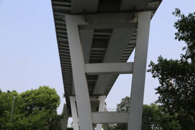 Bir üst geçidin beyaz çelik yapısı, yerden alınan iki simetrik sütun, ona bakıyor, mavi gökyüzüne ve Çin 'in batı göl parkındaki yeşil ağaçlara karşı.