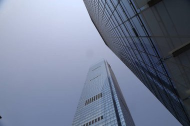 Dünyanın ikinci en yüksek binasının dış cephesi. Cam duvarlar ve sisli gökyüzüne uzanan çelik yapılar. Yerden görünüm