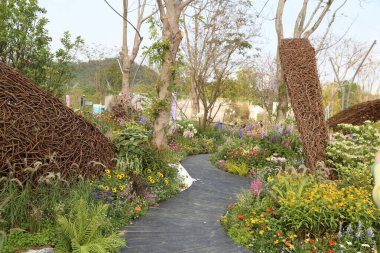 Doğada yetişen çeşitli çiçek ve bitkilerin yanı sıra ahşap ya da üzüm gibi doğal malzemelerden yapılmış yumurta şekilli büyük heykeller içeren organik bir bahçe tasarımı.