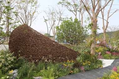 Bahçede ağaçlar ve çiçeklerle çevrili, sarmaşıklardan yapılmış dev bir ayakkabı şekilli heykel bulunmaktadır. Çevresindeki toprakta otlar, kır çiçekleri gibi çeşitli bitkiler var. Bu da doğayı andıran bir atmosfer yaratıyor.