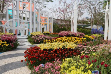 Çiçek fuarı bahçesinde renkli lalelerden ve kasımpatılardan oluşan, çeşitli çiçek türleriyle çevrili canlı bir atmosfer yaratan bir sanat kurulumu yer alıyor..