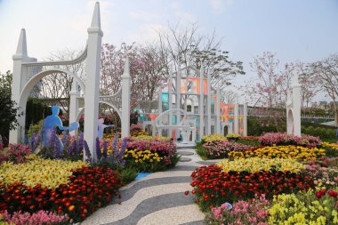 Açık hava çiçek fuarı, beyaz kemerli kapı unsurları ve çizgi film karakterleri şeklinde kurulum sanatı ile renkli çiçeklerin açık hava gösterimine sahiptir. Fotoğraf detayları yakalamak için geniş açı mercek kullanıyor.
