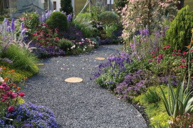 Mor, pembe, mavi, sarı, yeşil, beyaz, turuncu ve kırmızı tonlarda çeşitli çiçeklerle çevrili zarif ve renkli bir çiçek bahçesi..