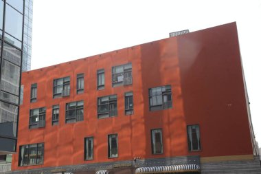 Kırmızı boyanmış binanın dışı, siyah pencereli ve beyaz duvarlı modern binalardan oluşmaktadır. Sağ üst köşede bir tarafında cam pencereler olan turuncu bir duvar var..