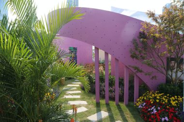 Pembe metalden kemerleri ve kenarlarında yeşil bitkiler ve renkli çiçeklerle çevrili delikleri olan mor, çağdaş bir bahçe..