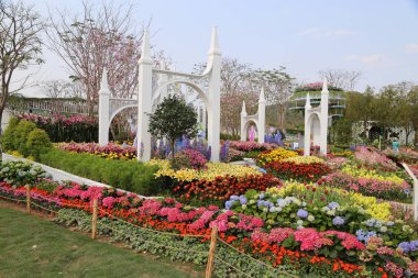 the flower show garden, with white arches and colorful flowers in front of them. the entire scene is surrounded by green lawns on both sides, creating an atmosphere full of vitality. in one corner there was also some trees that added depth to the ove