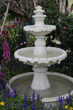 Canlı çiçekler ve yemyeşil yemyeşil ile çevrili, beyaz mermerden yapılmış zarif bir üç katlı çeşme, bahçe düzenine huzur katıyor. Fıskiyenin tasarımıyla ilgili karmaşık detaylara odaklanıyoruz..