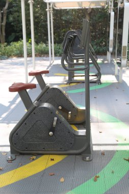 Açık hava fitness ekipmanları, parkta küçük bir spor salonu, dambılı ve egzersiz bisikleti, yeşil gri renkler, parlak çizgili kauçuk döşeme, doğal ışık
