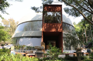 Büyük camları ve kırmızı çelik detayları olan origami kubbesi şeklinde yuvarlak bir modernist ev. Bina, bahçeler ve heykellerin yer aldığı yeşilliklerle çevrili..