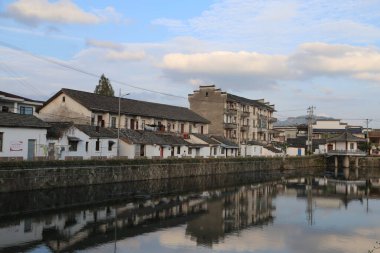 Beyaz duvarları ve siyah kiremitleri olan antik Çin 'in eski evleri, antik bir kasabada nehrin kıyısında dururlar, suyu yansıtırlar. Önünde başka bir caddeye uzanan basit binalarla dolu küçük bir köprü var..