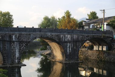 Antik Çin kasabasındaki nehrin üzerindeki taş kemer köprüsü, üzerinde üç ya da dört kemerli ve yanında iki ev bulunan küçük taşlardan yapılmıştır. Yanındaki eski binalarda siyah fayanslar ve beyaz duvarlar var..