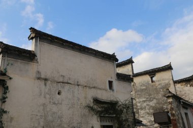 Çin 'in Jiangnan şehrindeki eski bir binanın resmi. Baharda mavi gökyüzü ve beyaz bulutlar. Duvarlarda yıpranmış boya var. Evin içinde ya da dışında kimse yok.