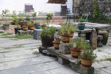 İçinde çeşitli otlar yetişen bir grup tencere, etrafında yeşillik olan eski bir Çin tarzı avlunun girişindeki taş masalar ve sandalyeler. Zemin gri tahta karolarla kaplıdır. Bir de açık hava yemek masası var.