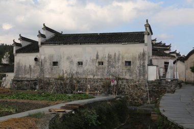 Çin 'in kırsal kesimlerinde, önünde sebze tarlalarıyla çevrili dört yan duvarlı beyaz duvarlı ve siyah kartonlu eski bir ev vardır. Ayrıca çatısı için daha fazla yer açmak için üzerine inşa edilmiş bir duvar da vardı..