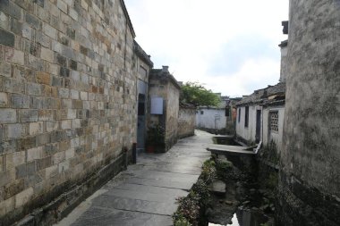 Her iki tarafında duvarlar ve ortasında küçük evler olan antik Çin köylerinin taşlarla döşenmiş yolları. Zemin gri tuğlalarla kaplı ve yanında başka bir sokağa açılan bir açıklık var.