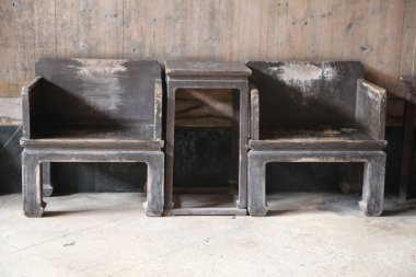 Koyu gri ahşaptan yapılmış ve kenarları geniş olan üç antik Çin sandalyesi, eski bir ahşap duvar arka planına karşı yan yana otururlar. Sandalyelerin sırtları süsleme ya da oyma olmadan düzdür..