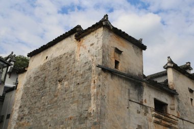 Geleneksel bir köy yapısının düşük açılı bir çekimi. Yaşlanmış, desenli duvarlar ve klasik koyu gri kiremitli çatı. Küçük ahşap pencereler ve solgun beyaz alçıyla kaplanmış yıpranmış dış görünüşü zengin bir mimarinin hikayesini anlatıyor.