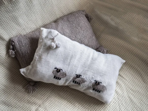 Two knitted pillows for home comfort, white pillow with sheep ornament.