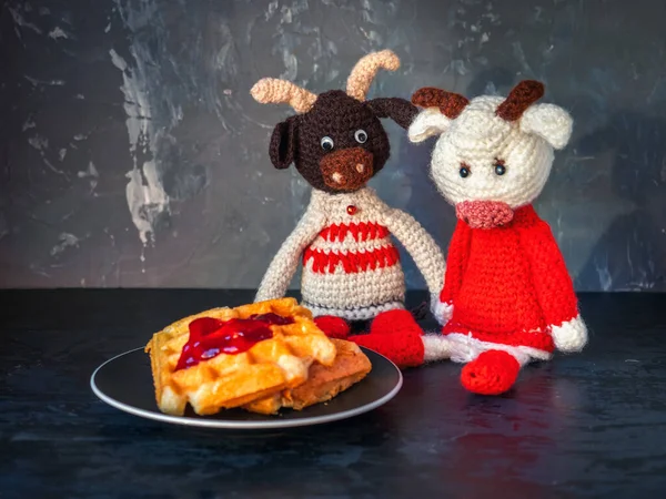 Couple of crocheted toys, elegant bulls sit near a saucer with a Christmas deck with cottage cheese waffles
