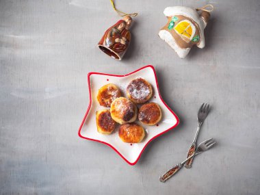 Pudra şekeri serpiştirilmiş peynirli kekler, dekoratif bir Noel tabağında frenk üzümü reçeli, gri arka planda Noel oyuncakları.