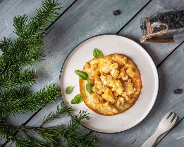 Protein kahvaltısı. Yuvarlak tabakta yumurta omletinde kızarmış tavuk eti. Yukarıdan bak. Köknar dallarıyla süslenmiş mavi bir tepside servis edilir.