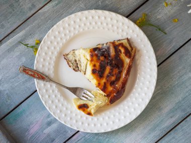 Beyaz yuvarlak tabakta, tatlı çatalı manzaralı süzme peynir güveci.