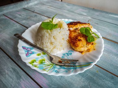 Pirinç yığını kaydırak ve tavuk pirzolası. Tahta tepside duran hafif bir tabakta taze bitki yaprakları.