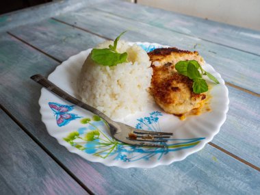 Pirinç yığını kaydırak ve tavuk pirzolası. Tahta tepside duran hafif bir tabakta taze bitki yaprakları.