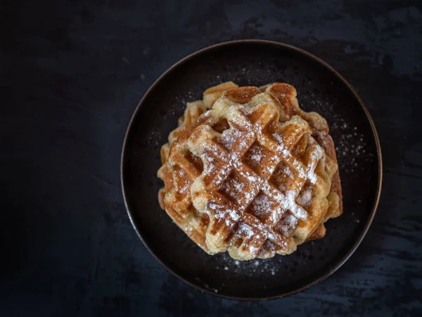 Gri arka planda siyah bir tabakta toz şekerli ev yapımı waffle 'lar.