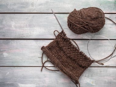 Yuvarlak örgü iğnelerinin üzerinde kahverengi iplikten örülmüş desenler yapıyorum.