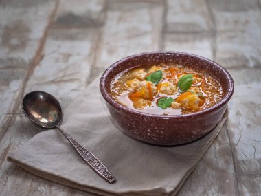 Sebzeli çorba ve kahverengi tabakta tavuk köftesi ve bir kaşık, açık masa üzerindeki keten peçete.