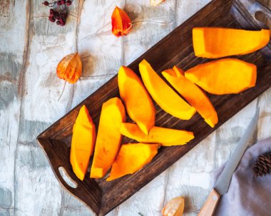 Dilimlenmiş çiğ balkabağı uzun bir ahşap tepside hafif bir masada, kurutulmuş bitki özü çiçekleri.