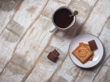 Hafif bir kahvaltı, kurabiyeler ve kahve. Protein bardağında, açık bir masanın üstünde.