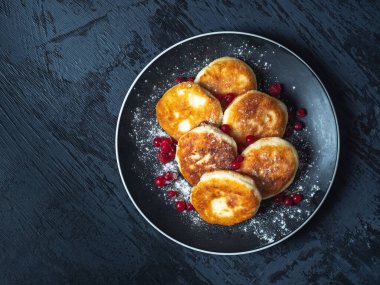 Siyah arkaplanda seramik tabakta pudra şekeri serpiştirilmiş peynirli kekler.