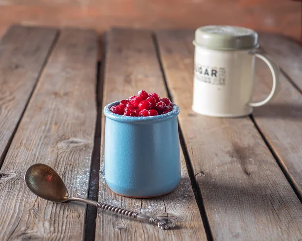 Cranberries with powdered sugar in a clay blue glass and powdered sugar in a tin can on a wooden table