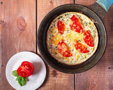 Domatesli omlet ve kızarmış tavada peynir ve beyaz tabakta yarım domates, kolay ve hızlı bir kahvaltı için ahşap tepside..