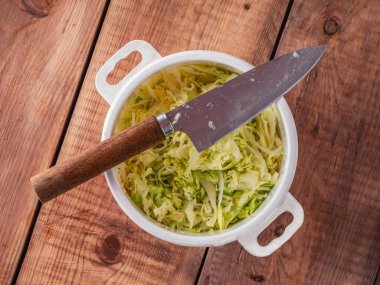 Salata hazırlama, plastik tencerede doğranmış taze lahana ve ahşap masada mutfak bıçağı.