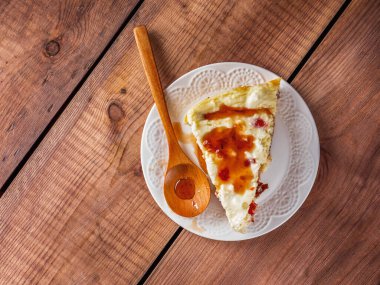 Beyaz tabakta böğürtlen şurubuyla süzme peynir güveci ve ahşap tepside ahşap kaşık.