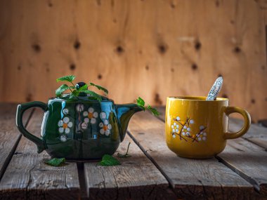 Yeşil seramik çaydanlıkta naneli çay ve ahşap masada çay bardağı.