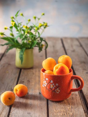 Turuncu bir kupada olgun kayısılar ve bir buket kır çiçeği, yeşil bir cam bardakta dravilat.