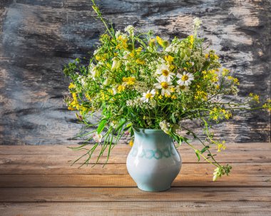 Tahta bir masanın üzerinde mavi bir vazoda kır çiçekleri.