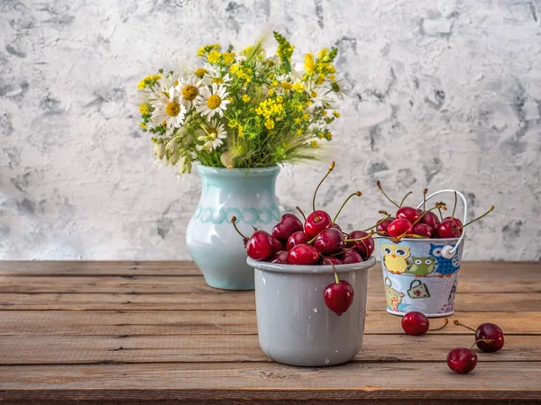 Naturaleza muerta de verano con cerezas y flores silvestres en un jarrón de campo sobre una mesa de madera — Foto de Stock