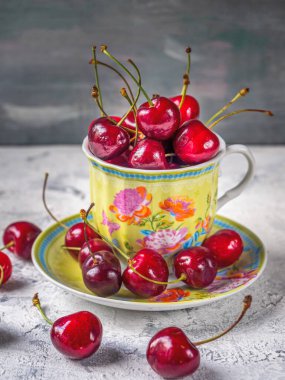 Sweet cherries in a mug with a floral pattern on a saucer on a light table close-up