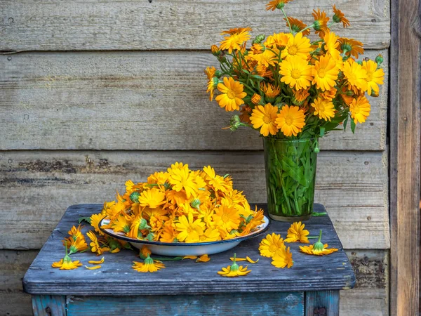 Ein Strauß Ringelblumen im Glas und gepflückte Blütenköpfe auf einem Teller — Stockfoto