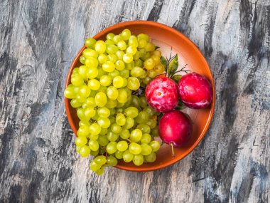 Kiş-fare üzümleri ve kil bir tabakta kırmızı erikler, üst görünüm kapalı